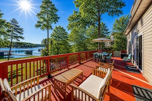 A deck with outdoor furniture, a view of a lake, and a building with a red railing.