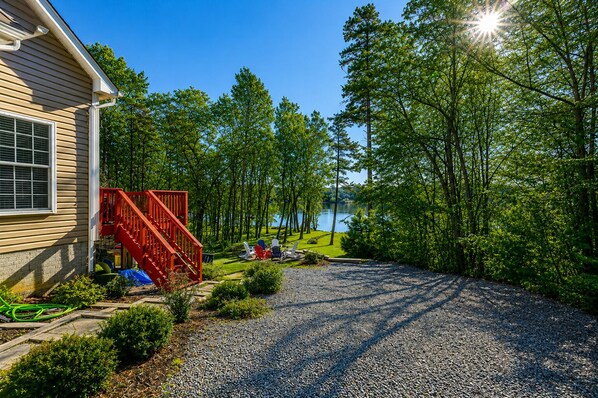 A house with a gravel driveway, a red staircase, and a view of a lake surrounded by trees.