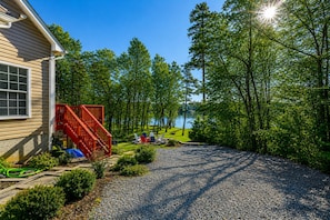 A house with a gravel driveway, a red staircase, and a view of a lake surrounded by trees.