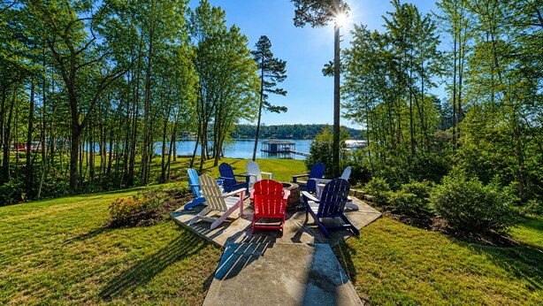 Ein Seeufer mit einer Holzterrasse, Adirondack-Stühlen, einem Betonweg und Blick auf einen See und eine Anlegestelle.