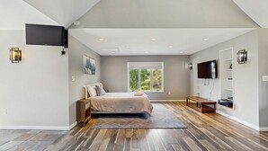 A bedroom with a bed, a TV mounted on the wall, a window, and a wooden floor.