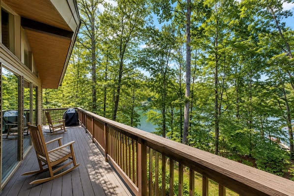 Eine Holzterrasse mit Geländer, die auf einen See mit umliegenden Bäumen blickt.