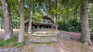 Un'ampia casa a più piani in legno, circondata da alberi, con un vialetto in pietra che conduce all'ingresso.