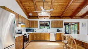 Cucina con mobili in legno, frigorifero in acciaio inossidabile, ventilatore a soffitto e un'ampia finestra.