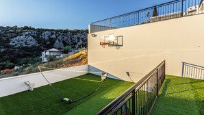 A modern building with a rooftop tennis court, a balcony, and a view of a hilly landscape. - Villa La Fortezza With sea View (Marina)