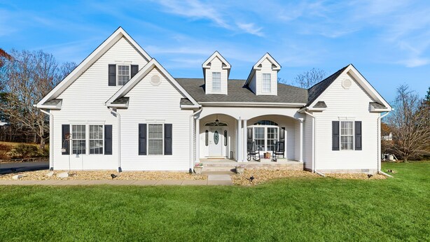 A two-story white house with a central entrance, a covered porch, and a well-maintained lawn. - Peaceful lakeside retreat with hot tub, private pool, dock & paddle boards (Orange)