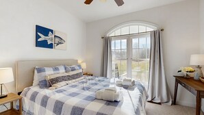 A hotel room with a large bed, a window with curtains, a desk with a lamp, and artwork on the wall. - Peaceful lakeside retreat with hot tub, private pool, dock & paddle boards (Orange)