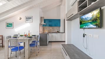 Una cucina moderna con piano cottura integrato, un'area pranzo con sedie blu e un grande televisore a schermo piatto montato a parete.