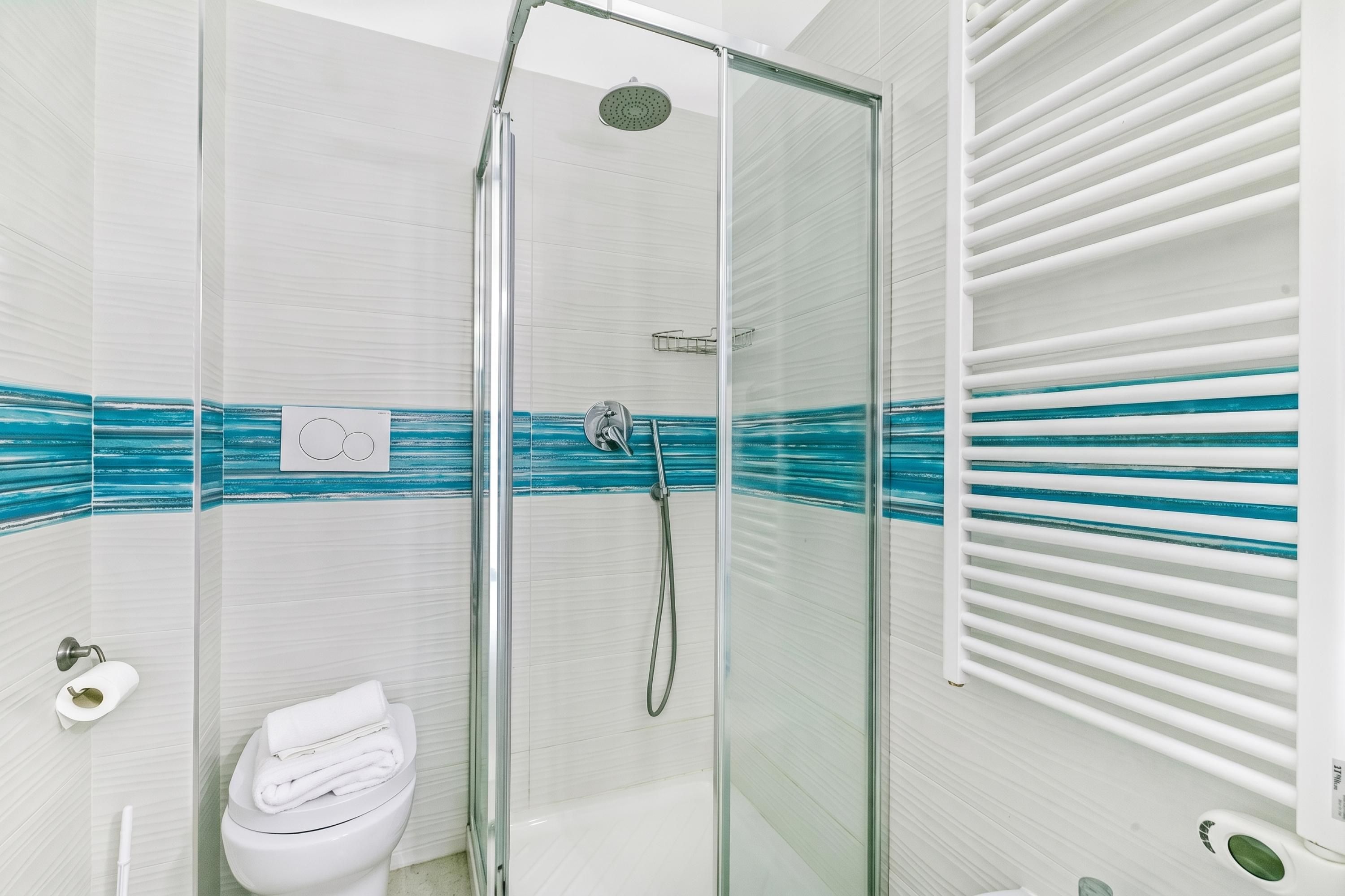A modern bathroom with a glass-enclosed shower, a toilet, and a towel rack.