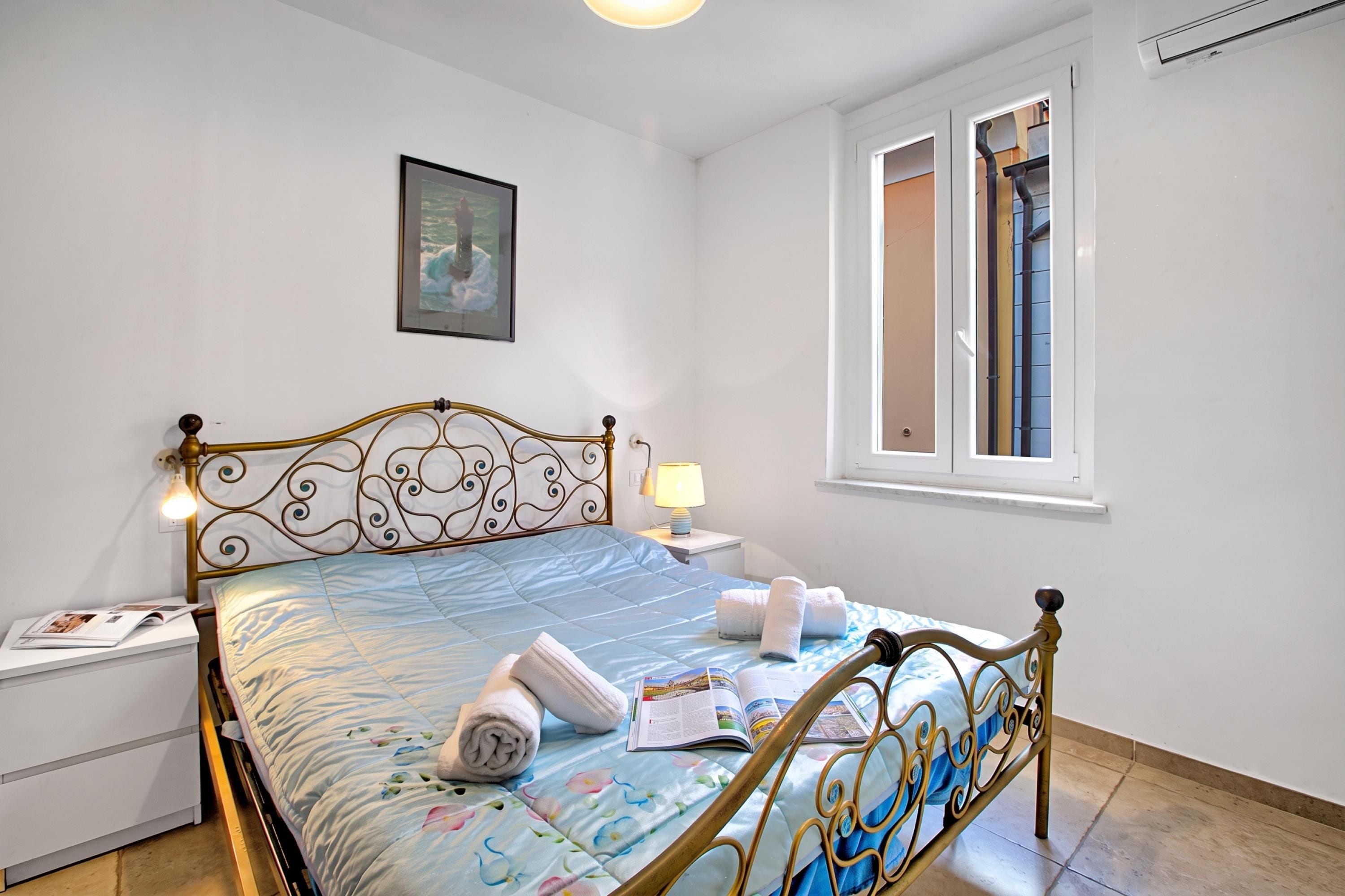 A neatly made bed with a blue floral bedspread, a bedside lamp, and a framed picture on the wall.