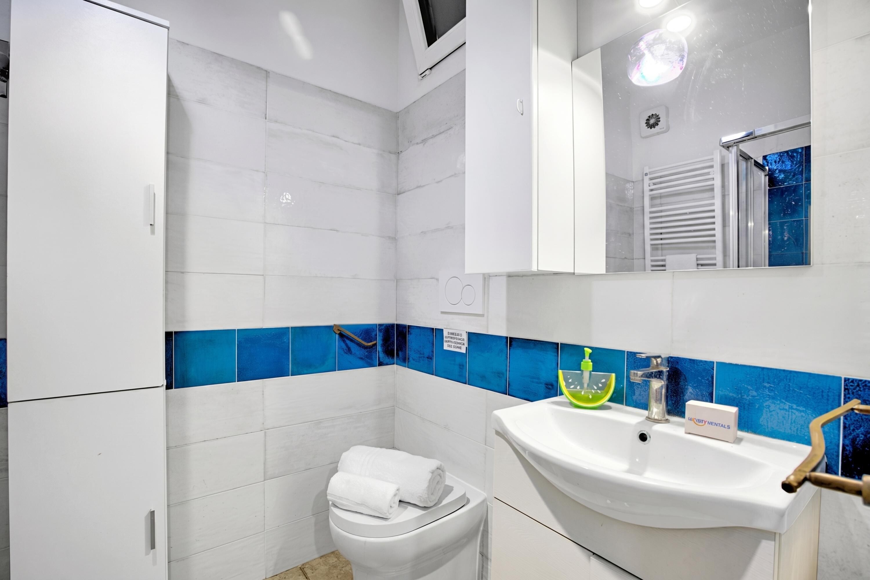 Un baño con inodoro blanco, lavamanos con dispensador de jabón y espejo sobre el lavamanos.