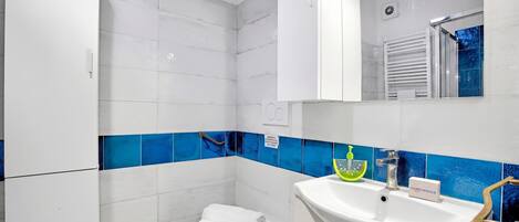 Un baño con inodoro blanco, lavamanos con dispensador de jabón y espejo sobre el lavamanos.