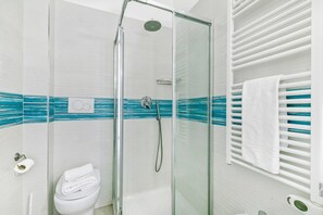 Une douche en verre avec un pommeau de douche à main, des toilettes blanches et un porte-serviettes avec une serviette blanche.