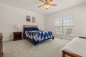 A bedroom with a bed, a nightstand, a lamp, a ceiling fan, and a window with blinds.