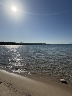 A beach with clear water reflecting sunlight, a sandy shore, and distant hills. - Peaceful Riverfront Retreat. Fall Color, Fishing, Kayaks, Fire Pit. Dogs Welcome (Beulah)