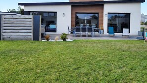 Una casa moderna a due piani con tetto piatto, ampie finestre e un patio con posti a sedere all'aperto.