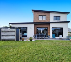 A modern two-story house with a flat roof, large windows, and a patio area with outdoor seating. - Villa Odeven 300 m from the sea Holim'Prest (Cléder)