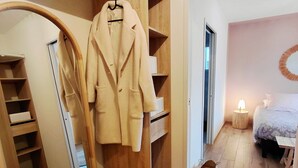 Una camera da letto con pavimento in legno, un letto con copripiumino floreale, un comodino con lampada e un armadio con cappotto appeso.