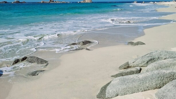 Una spiaggia sabbiosa con grandi rocce e acque oceaniche calme.