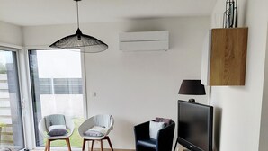 Un soggiorno moderno con un divano, poltrone, un tavolino in vetro, una TV e un mobile contenitore in legno.