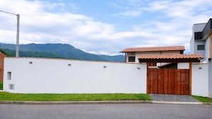 A modern house with a white exterior, a wooden gate, and a mountain backdrop. - Swallows. Charming suite, swimming pool. Close to everything (Paraty)