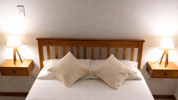 A neatly made bed with a wooden headboard, two bedside lamps, and a rolled towel on the bed. - Swallows. Charming suite, swimming pool. Close to everything (Paraty)