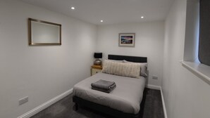 Een slaapkamer met een bed, nachtkastje, lamp, spiegel en kunst aan de muur.