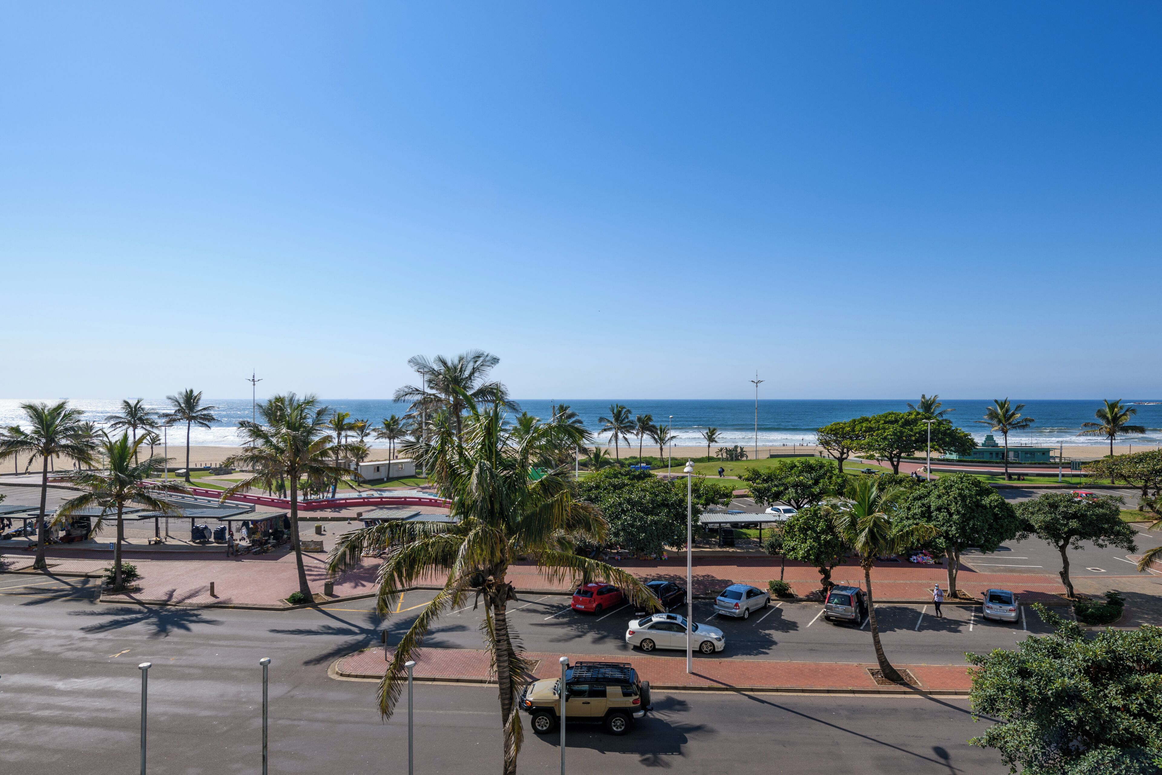 A parking lot with cars, palm trees, and a beach view.