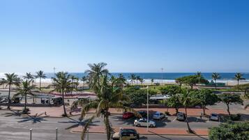 A parking lot with cars, palm trees, and a beach view.