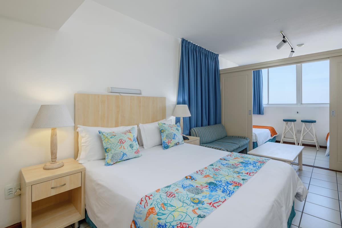 A hotel room with a bed, two bedside tables, a desk, a chair, a window, and a curtain.