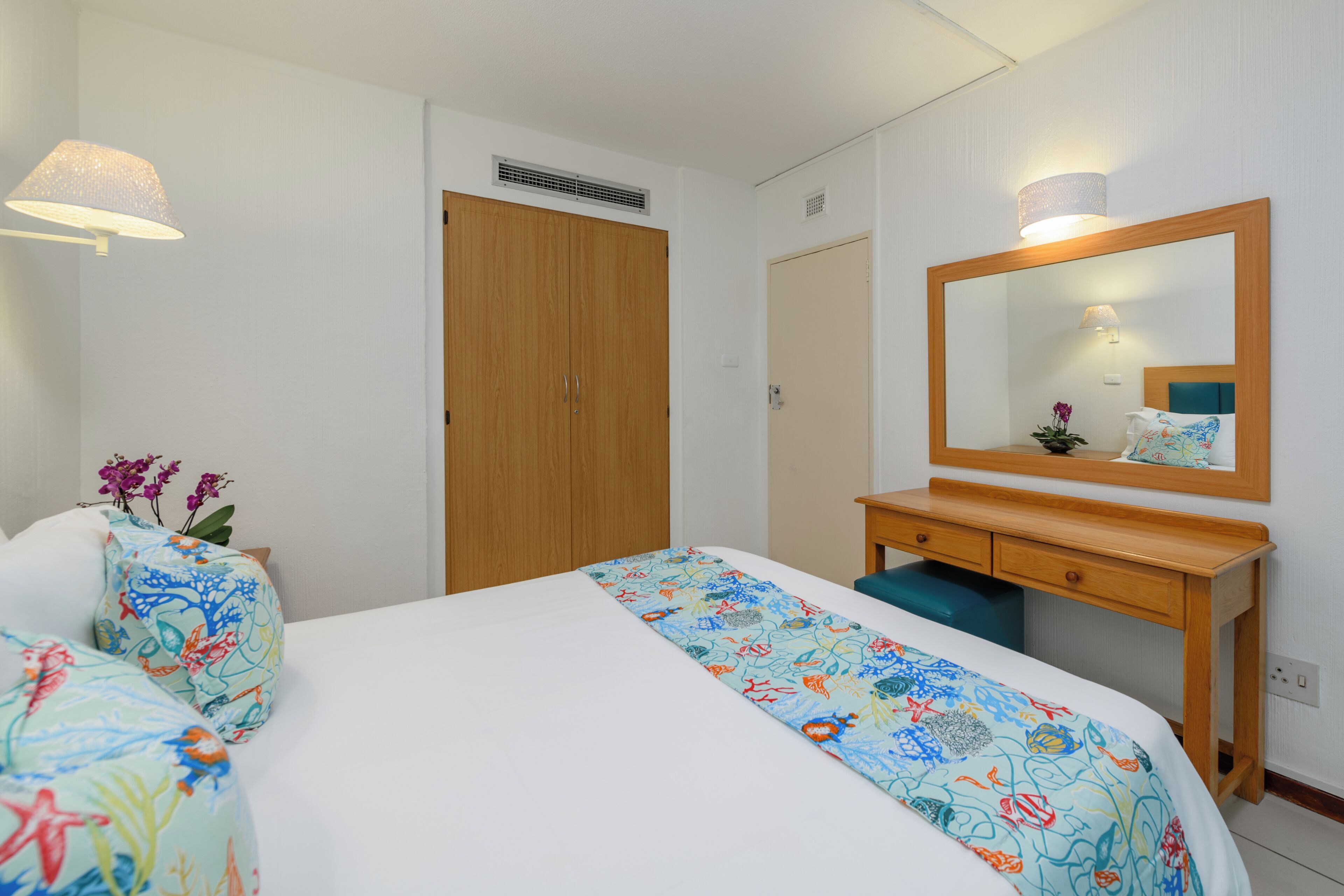 A hotel room with a bed, a wooden dresser, a mirror, and a window.