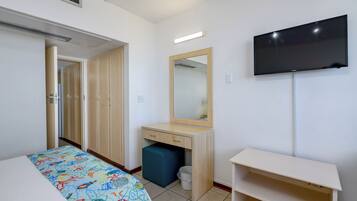 A hotel room with a bed, a desk with a mirror, a television, and a wardrobe.