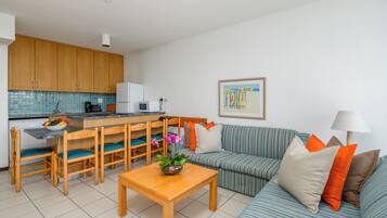 Una cocina moderna con armarios de madera, una zona de comedor con sillas y una mesa, un sofá a rayas con cojines, y un cuadro enmarcado en la pared.