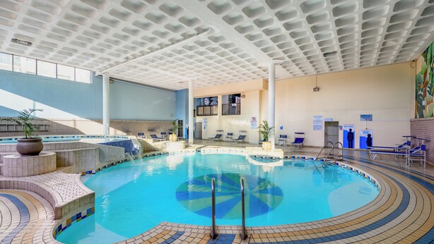 An indoor swimming pool with a tiled floor, a ceiling with a grid pattern, and a few lounge chairs. - Durban Spa (Durban)