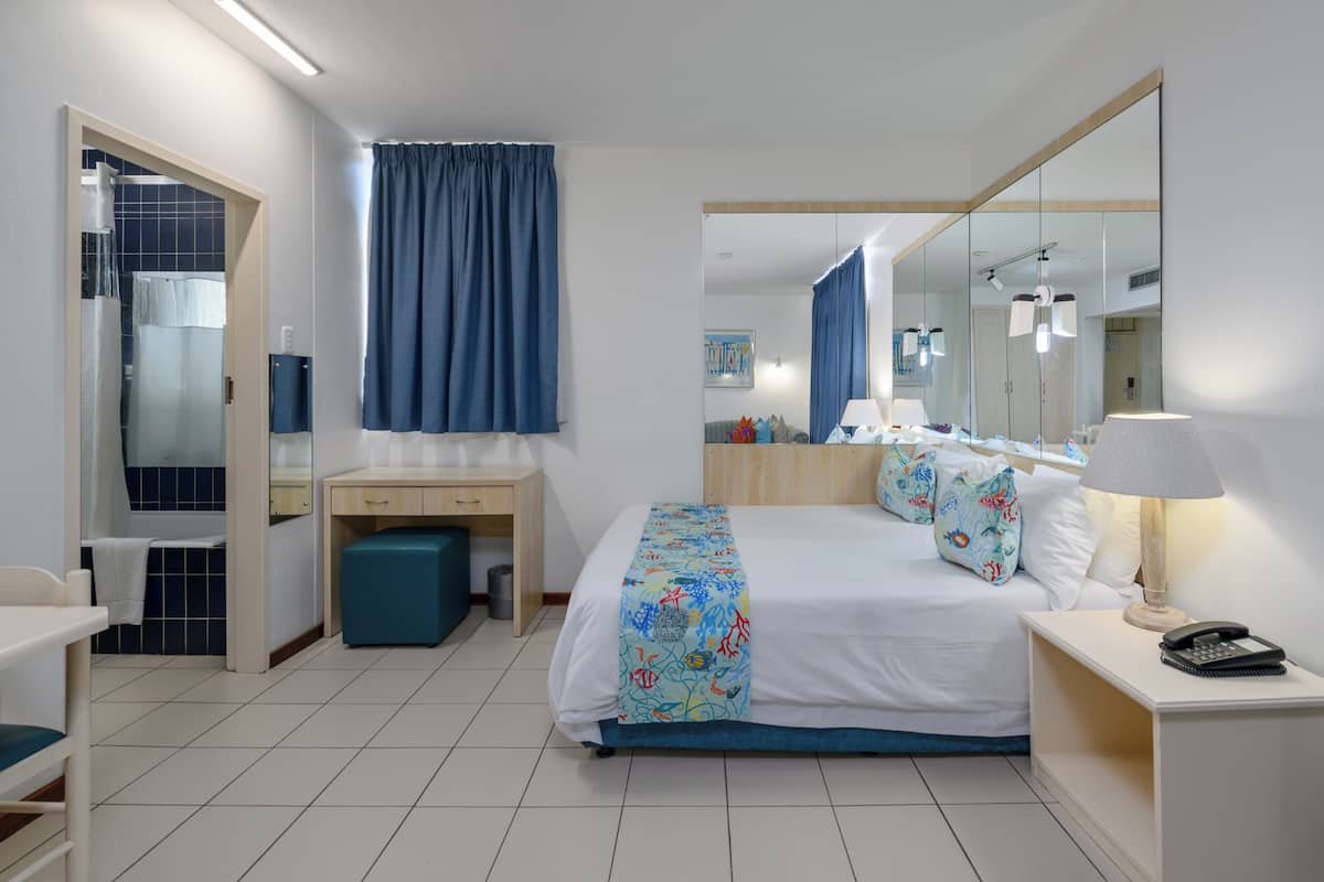 A hotel room with a bed, bedside table, desk, chair, and a bathroom with a shower and toilet.