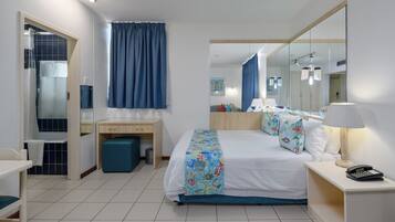 A hotel room with a bed, bedside table, desk, chair, and a bathroom with a shower and toilet.