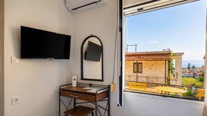 Een kamer met een bureau, stoel, televisie en een raam met uitzicht op gebouwen.