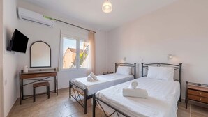 Een slaapkamer met twee bedden, een bureau, een televisie en een raam met uitzicht op gebouwen.