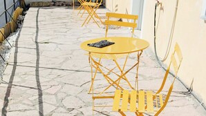 Een binnenplaats met terras, een gele emmer en een gebouw met een raam.