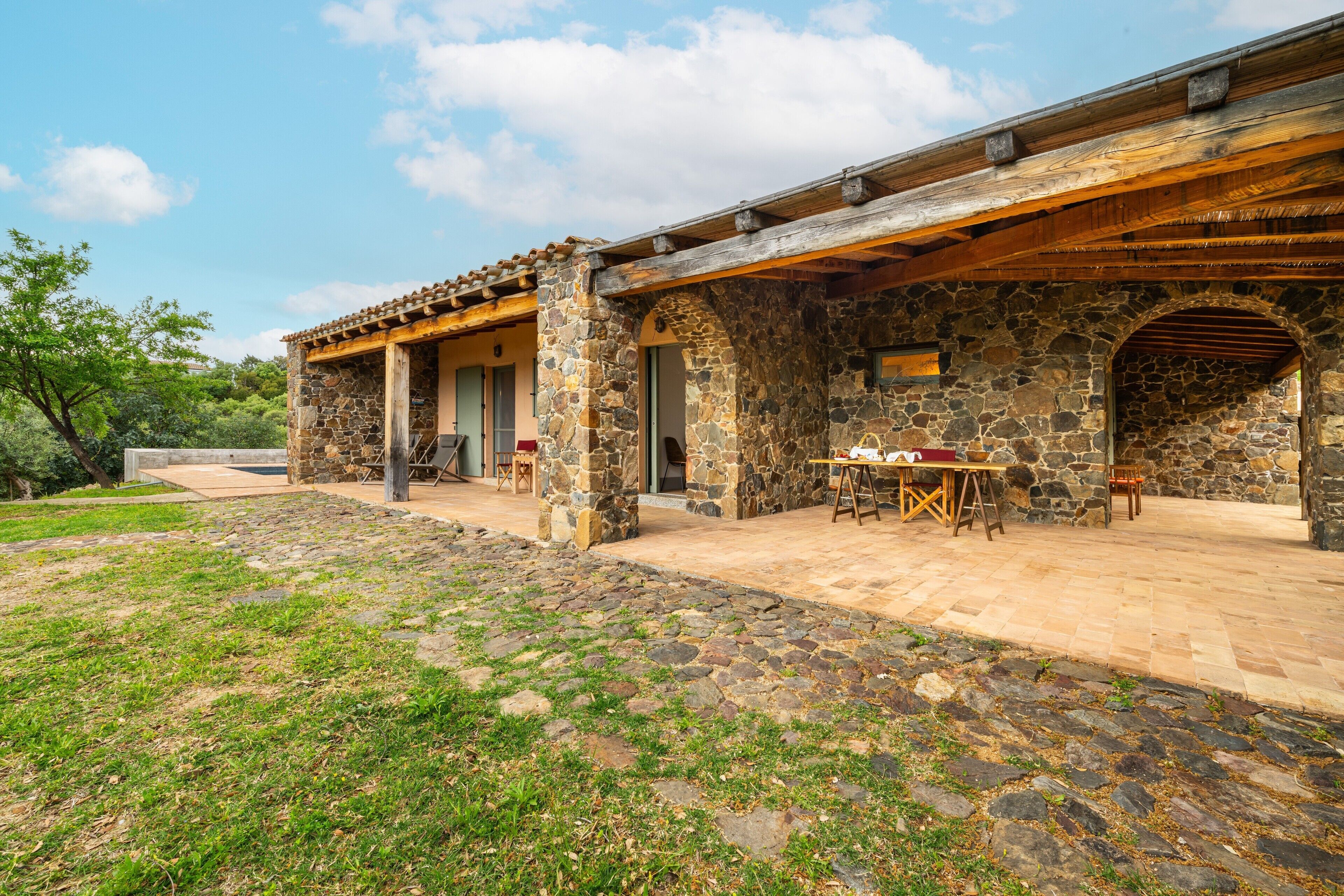 Ein Steinhaus mit einer überdachten Terrasse, Sitzgelegenheiten im Freien und einem Kiesweg.