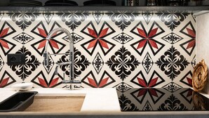 A kitchen with a patterned backsplash, a stainless steel faucet, and a wooden cutting board.