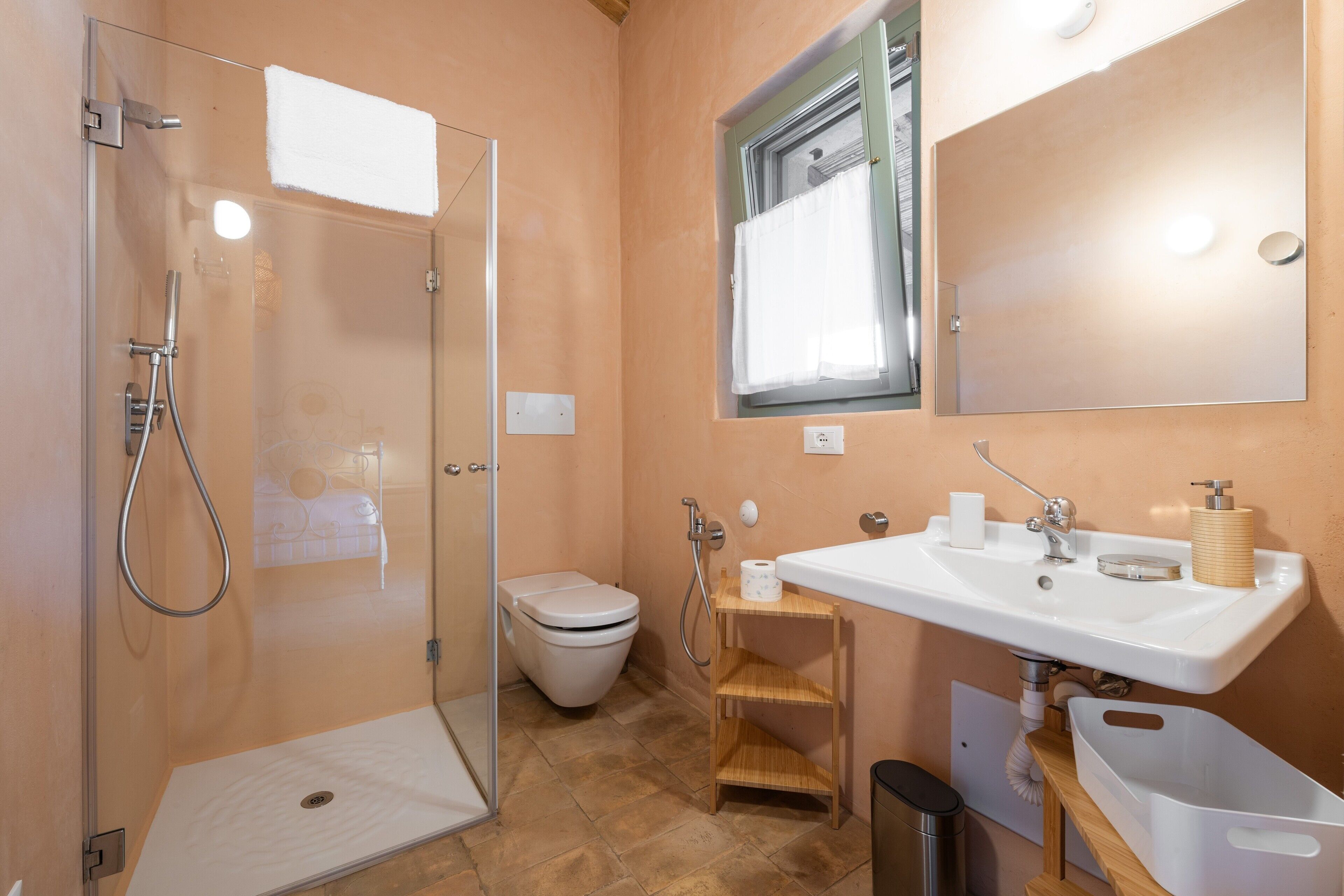 A bathroom with a glass shower enclosure, a toilet, a sink, and a mirror.