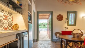 A kitchen with a built-in dishwasher, a dining area with a wooden table and chairs, and a view through an open doorway to an outdoor area.