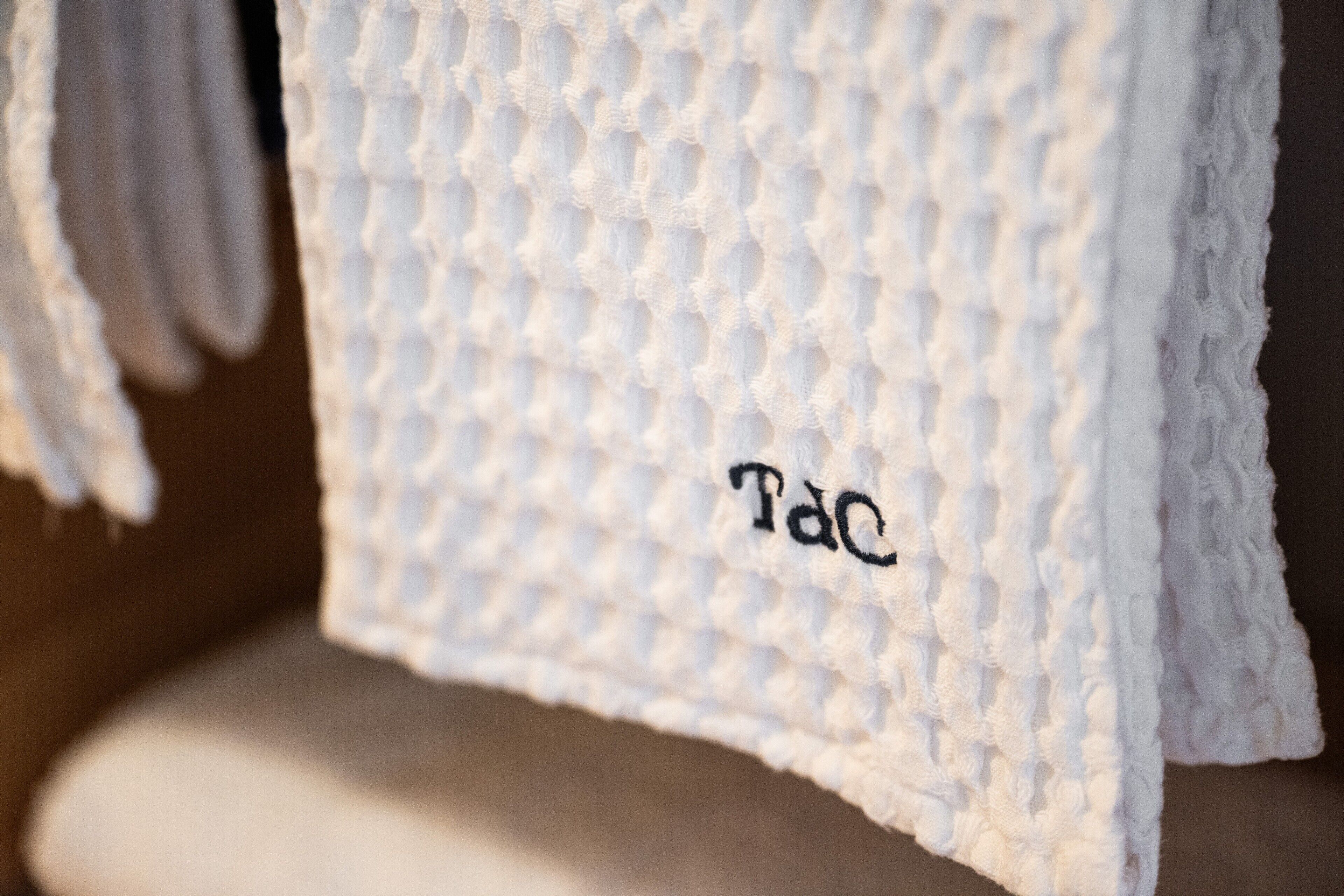 Ein weißes, strukturiertes Handtuch mit 'TaC'-Stickerei.