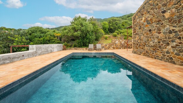 A rectangular swimming pool with clear blue water, surrounded by a stone wall and a wooden deck.
