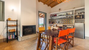 A kitchen with a fireplace, wooden dining table, and orange chairs. - La Tanca Del Conte - Suite Banano: Private Pool, Sea View, Nature Retreat (Muravera)