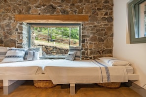 Ein Zimmer mit Steinwänden, einem Bett, einem Fenster und einem Holzbalken darüber.
