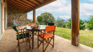 Een terras buiten met een stenen muur, houten stoelen, een tafel en uitzicht op het landschap.