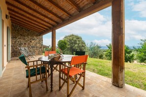 Une terrasse extérieure avec un mur en pierre, des chaises en bois, une table et une vue sur le paysage.