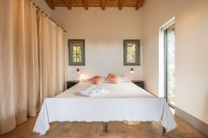 Une chambre à coucher avec un lit, deux tables de chevet, une fenêtre et un rideau.